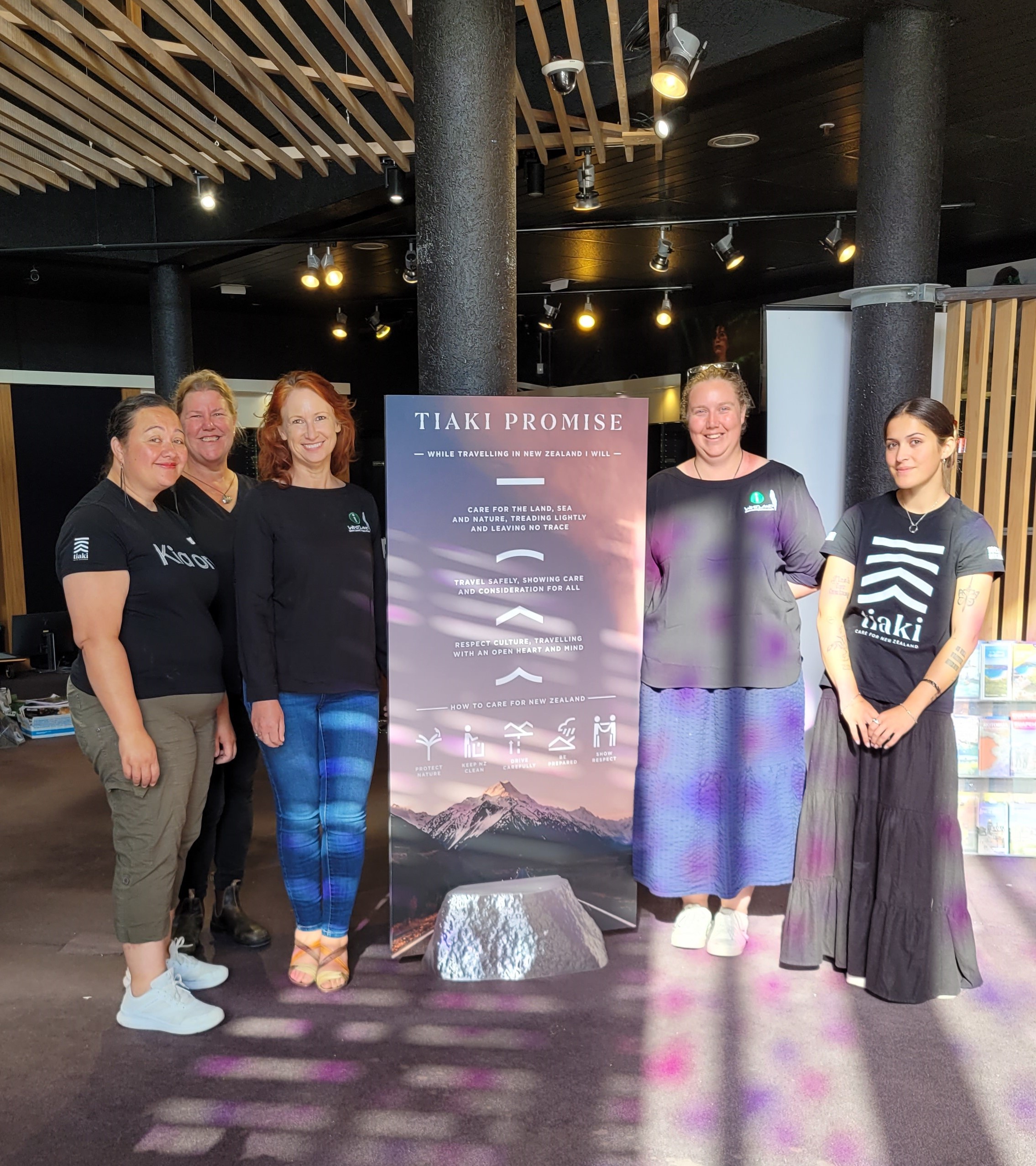 5 women standing by a large sign in black isite uniforms