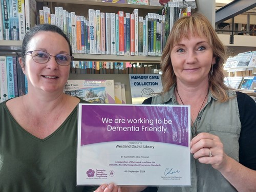 Two women in a library holding a certificate